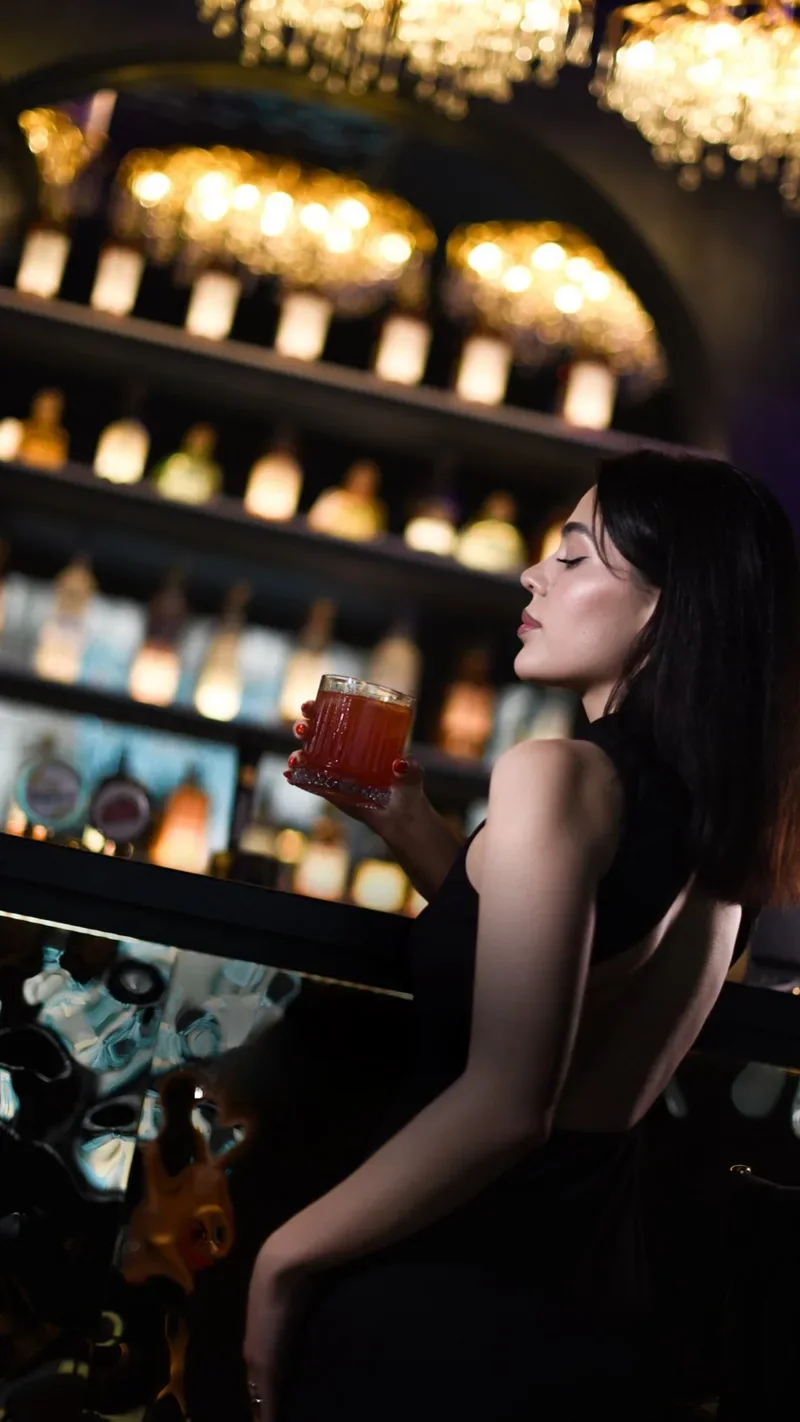 A guest with a cocktail against the bottle shelves